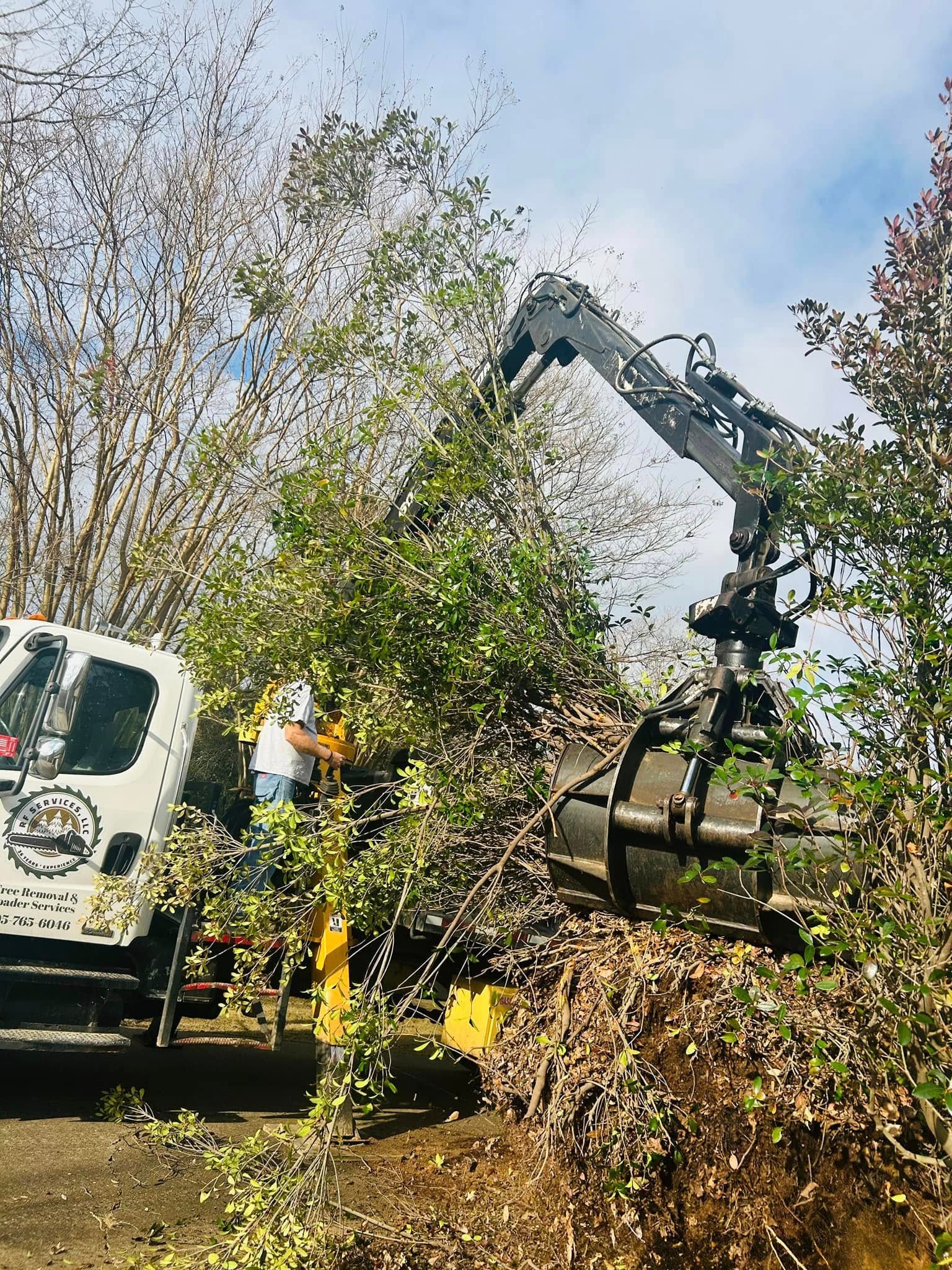 RF Services grapple loader lifting uprooted shrub with branded truck